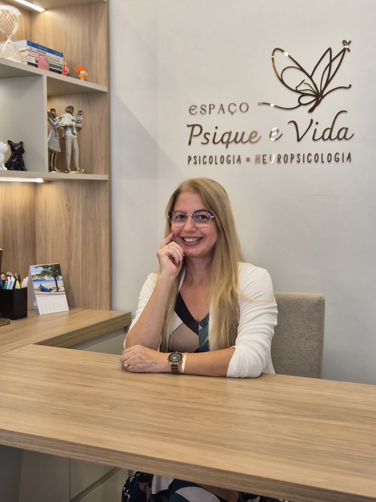 Viviane Gatis à mesa do consultório, apoiando o rosto na mão e sorrindo.